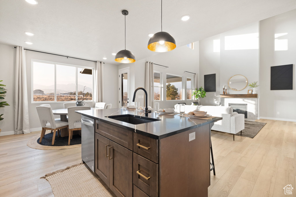 Kitchen with dark brown cabinetry, an island with sink, sink, decorative light fixtures, and light wood-type flooring