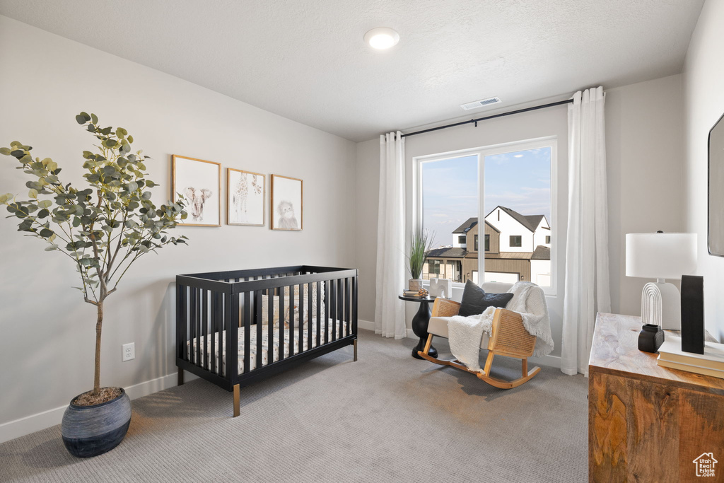 Bedroom featuring a textured ceiling, a crib, and carpet