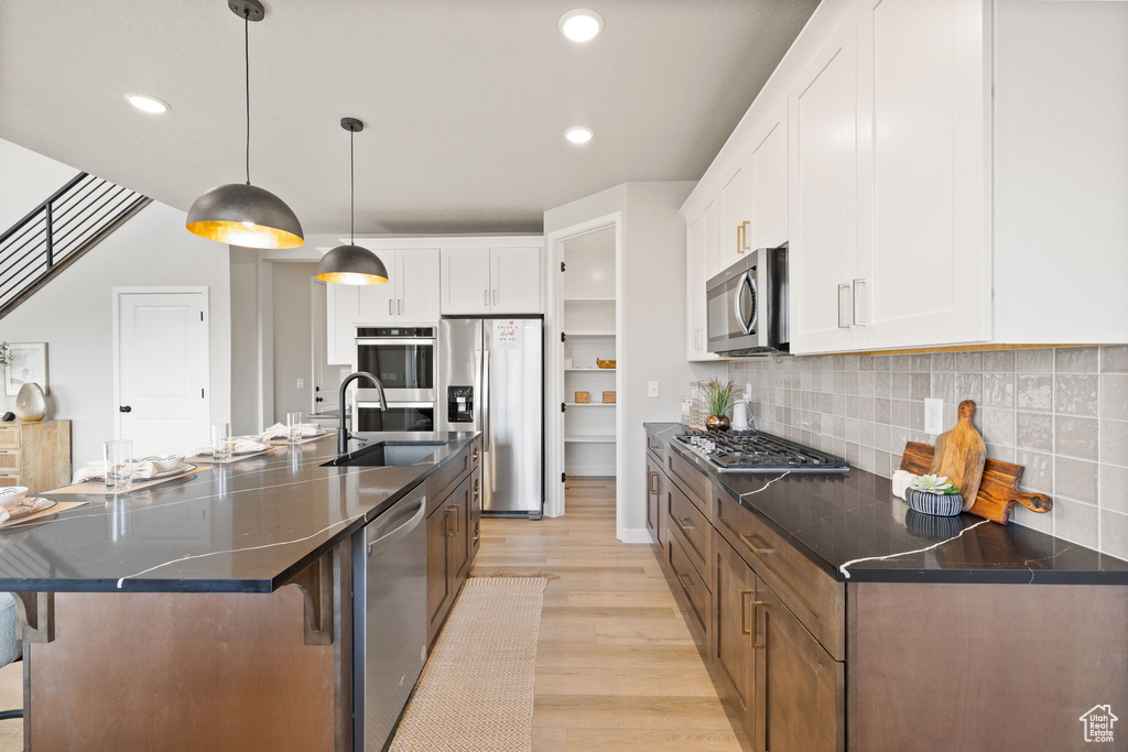 Kitchen with pendant lighting, white cabinets, an island with sink, and appliances with stainless steel finishes