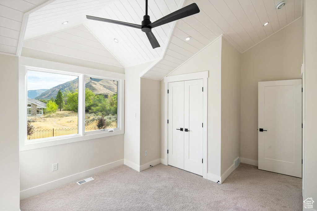 Unfurnished bedroom with ceiling fan, a mountain view, light colored carpet, and lofted ceiling