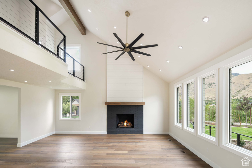 Unfurnished living room with high vaulted ceiling, a large fireplace, ceiling fan, and plenty of natural light