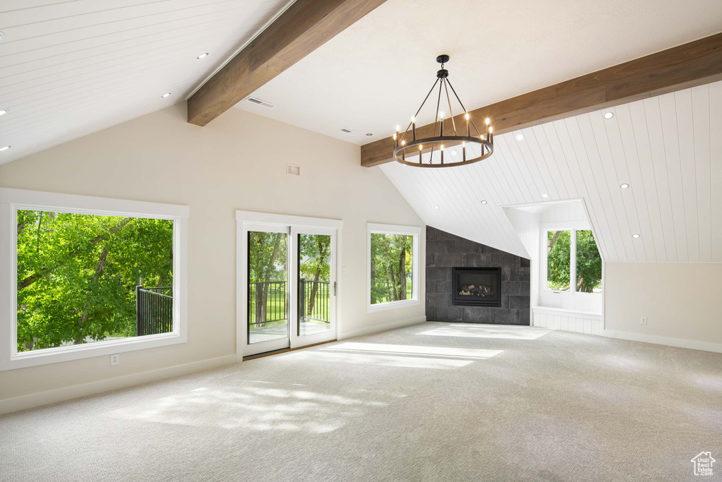 Unfurnished living room with a tile fireplace, carpet flooring, lofted ceiling with beams, and a notable chandelier