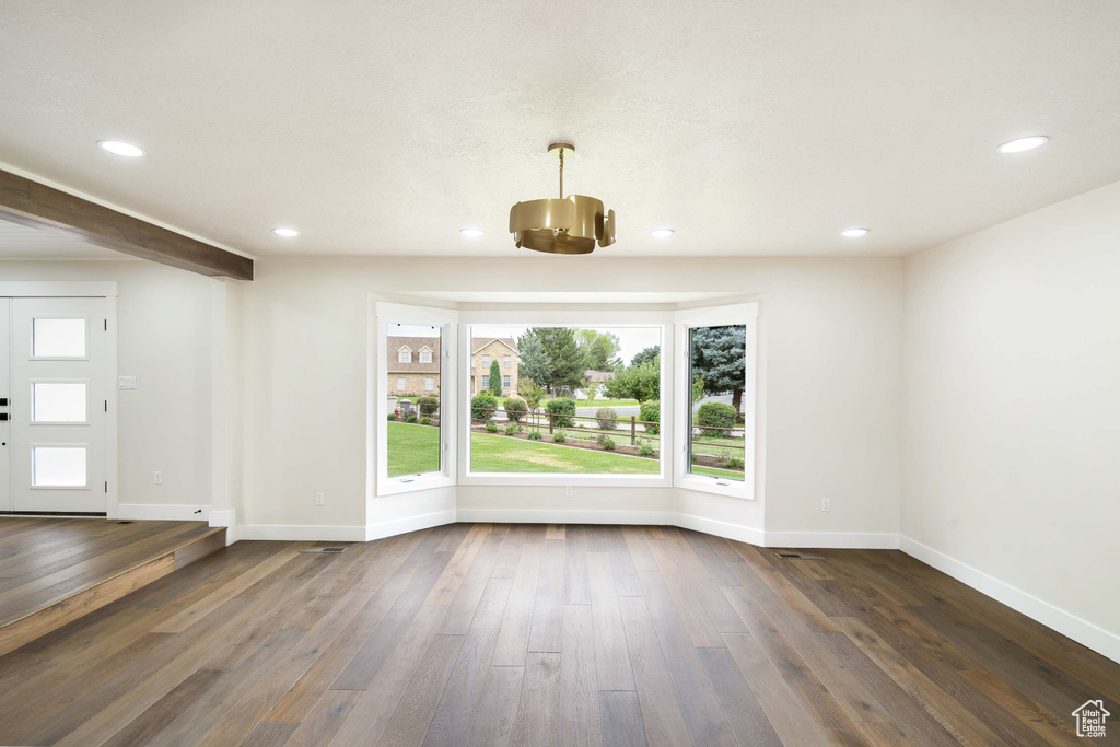 Empty room with a notable chandelier, beam ceiling, and dark hardwood / wood-style floors