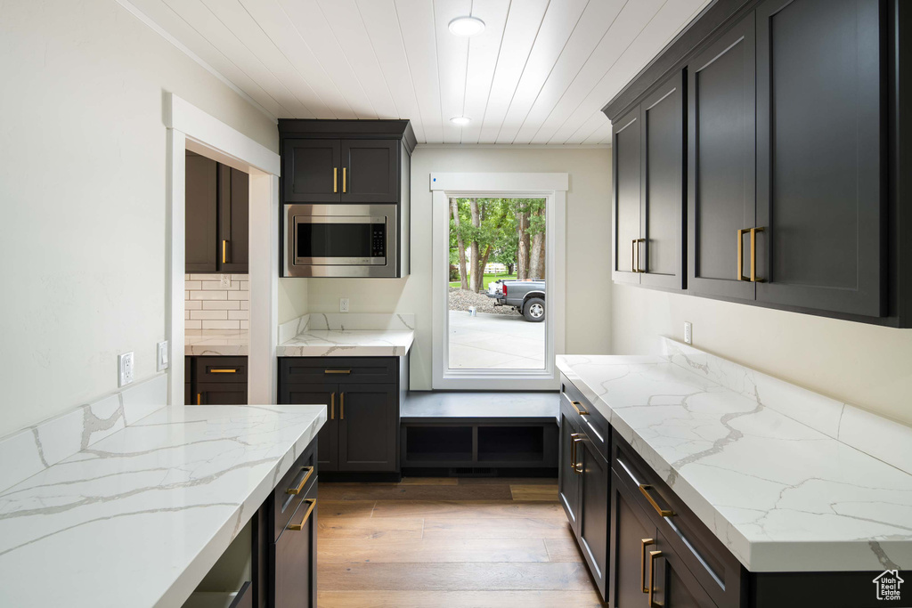 Kitchen featuring wood ceiling, stainless steel microwave, light hardwood / wood-style flooring, and light stone counters