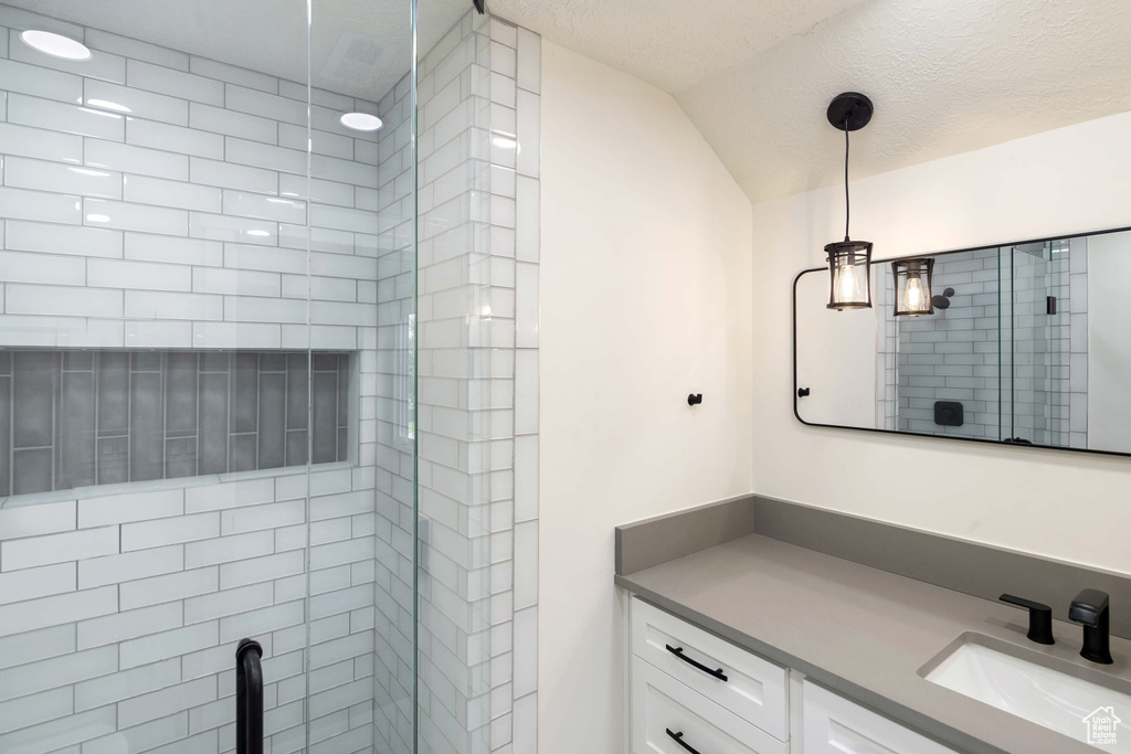 Bathroom with a textured ceiling, a tile shower, lofted ceiling, and vanity