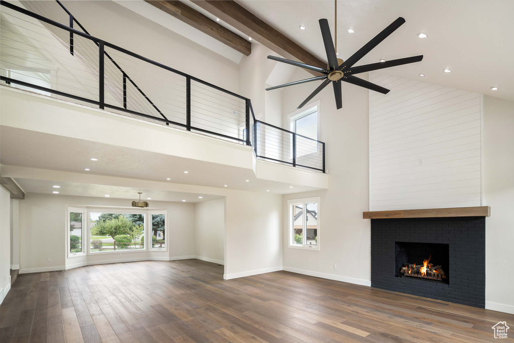 Unfurnished living room with beamed ceiling, a fireplace, high vaulted ceiling, dark hardwood / wood-style flooring, and ceiling fan