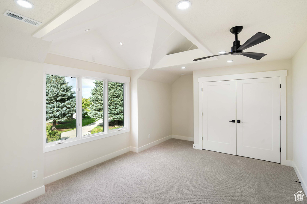 Unfurnished bedroom featuring lofted ceiling with beams, a closet, ceiling fan, and light carpet