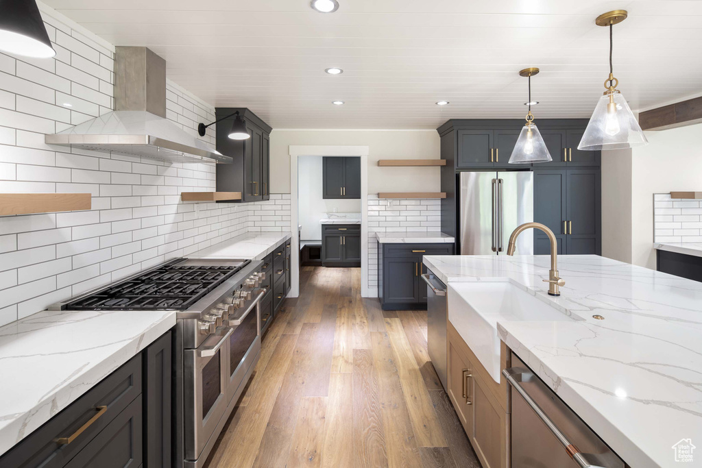 Kitchen with hardwood / wood-style flooring, wall chimney range hood, premium appliances, backsplash, and decorative light fixtures