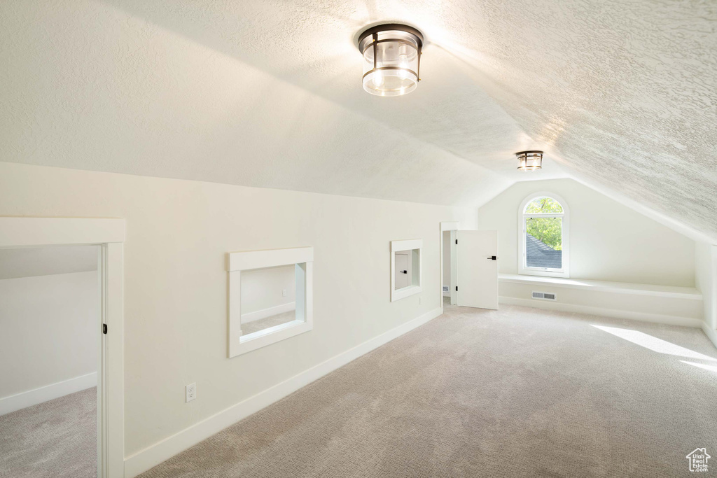 Additional living space with light colored carpet, a textured ceiling, and lofted ceiling