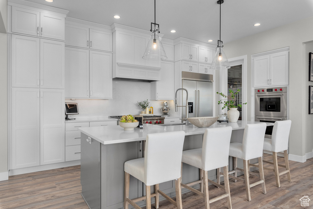 Kitchen featuring white cabinets, pendant lighting, a center island with sink, stainless steel appliances, and a kitchen bar