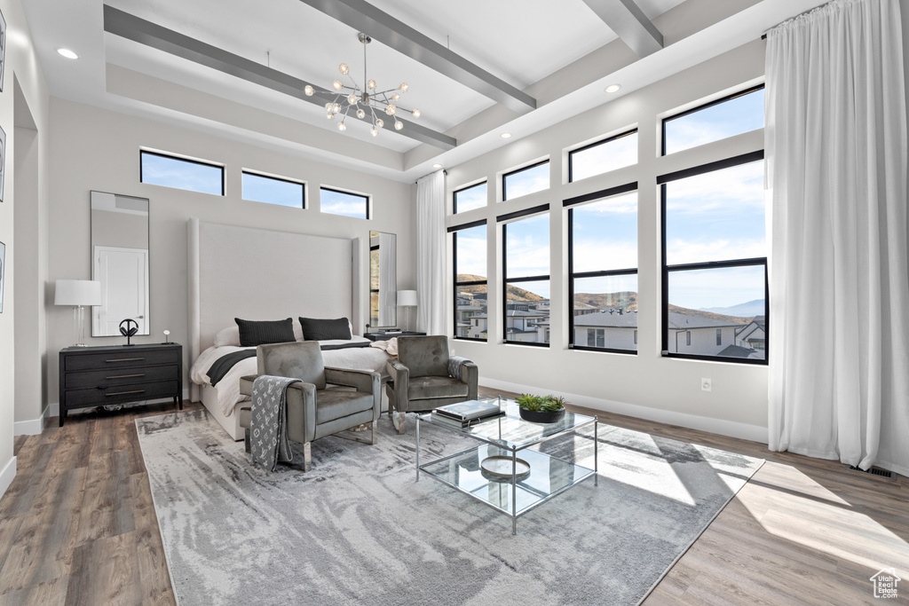 Bedroom with an inviting chandelier, a towering ceiling, hardwood / wood-style floors, and multiple windows