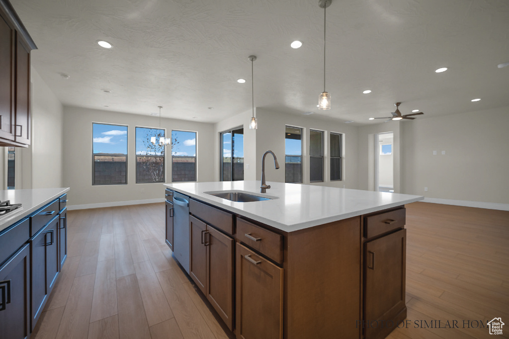 Kitchen with ceiling fan with notable chandelier, pendant lighting, light wood-type flooring, a kitchen island with sink, and sink