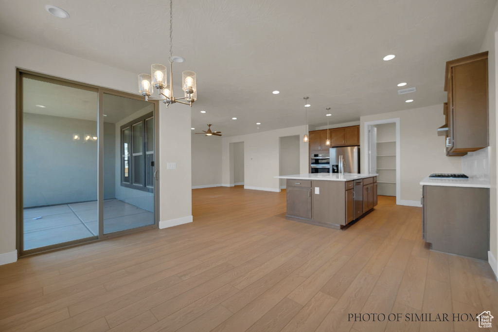 Kitchen featuring appliances with stainless steel finishes, light wood-type flooring, pendant lighting, and an island with sink