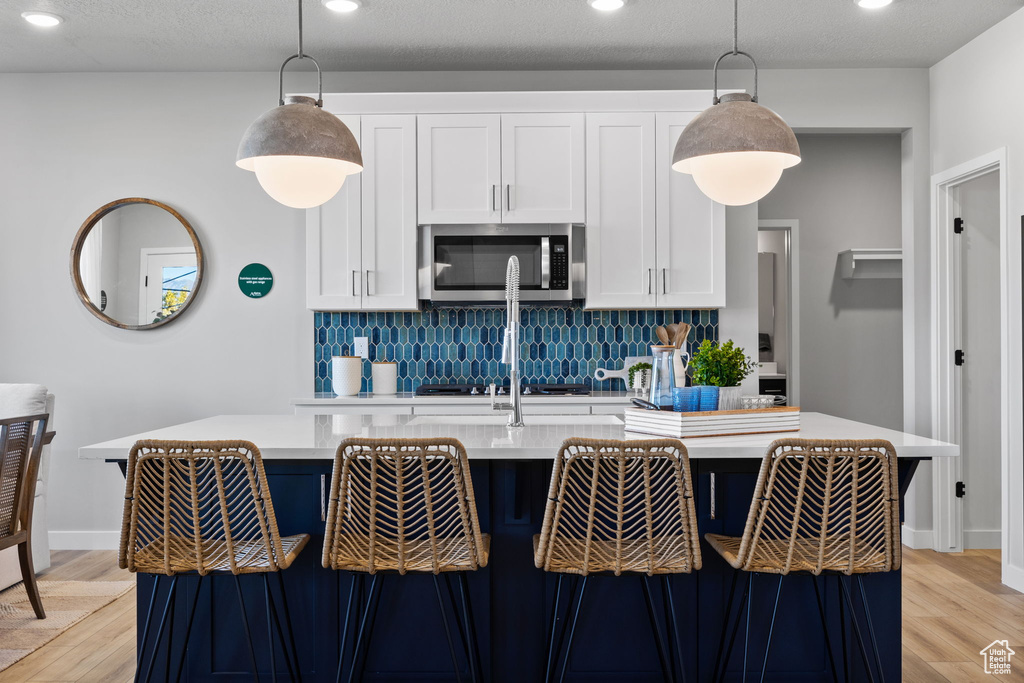 Kitchen with hanging light fixtures, a kitchen island with sink, light hardwood / wood-style flooring, and stainless steel appliances