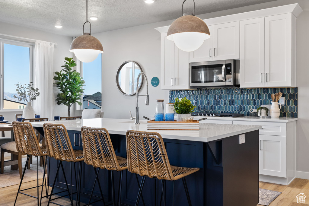 Kitchen featuring white cabinets, a kitchen island with sink, hanging light fixtures, and light hardwood / wood-style floors