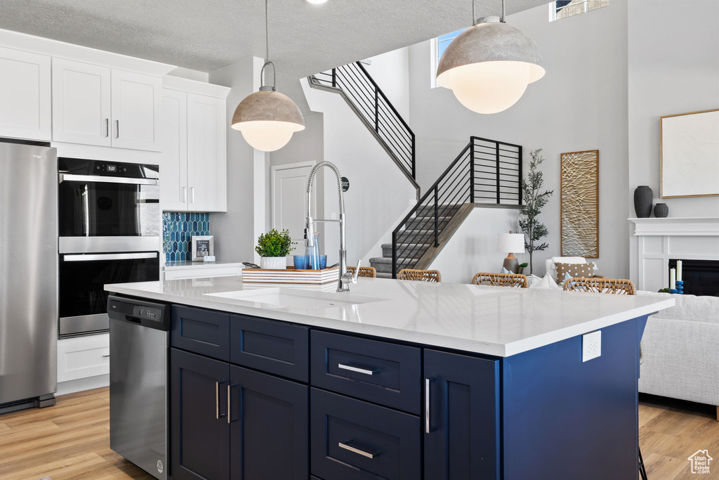 Kitchen with appliances with stainless steel finishes, hanging light fixtures, a textured ceiling, and light hardwood / wood-style flooring