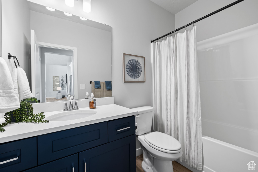 Full bathroom with vanity, hardwood / wood-style floors, toilet, and shower / bathtub combination with curtain