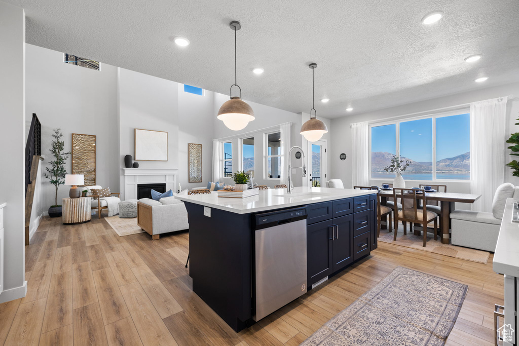 Kitchen with a healthy amount of sunlight, dishwasher, an island with sink, and decorative light fixtures