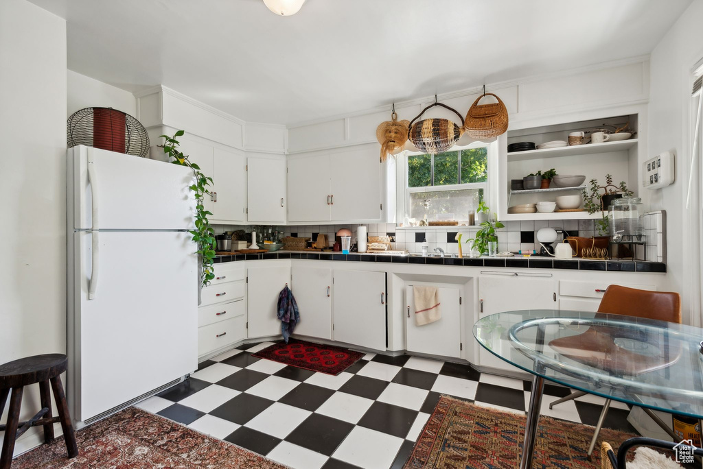 Kitchen with white cabinets, white refrigerator, tile countertops, and backsplash