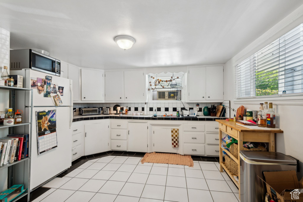 Kitchen featuring decorative backsplash, white cabinets, tile counters, and white fridge