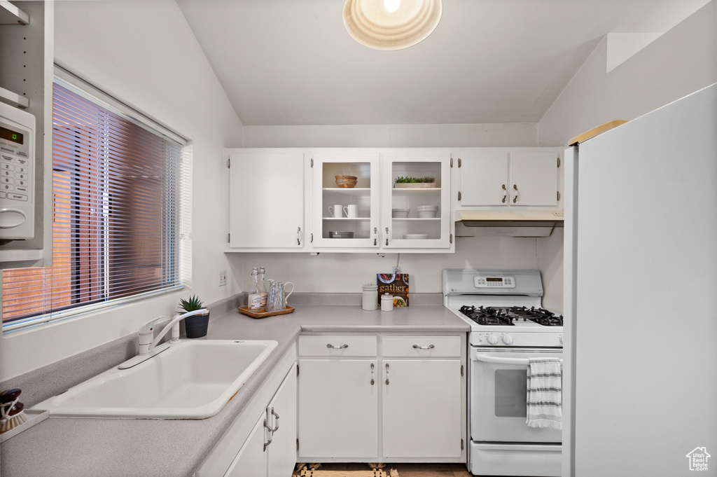 Kitchen with white cabinets, white appliances, vaulted ceiling, and sink