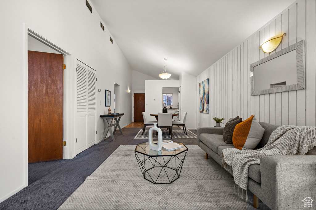 Living room featuring wood walls, dark colored carpet, and high vaulted ceiling