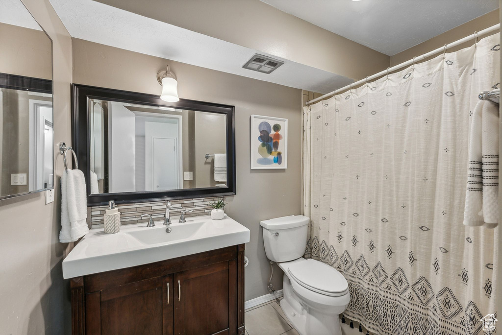 Bathroom featuring tasteful backsplash, a shower with shower curtain, tile patterned floors, vanity, and toilet