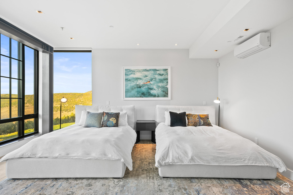 Bedroom featuring a wall mounted air conditioner, multiple windows, and wood finished floors