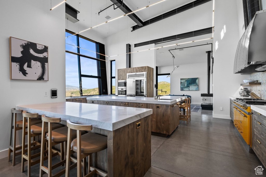 Kitchen with a towering ceiling, an island with sink, high quality fridge, modern cabinets, and a kitchen breakfast bar