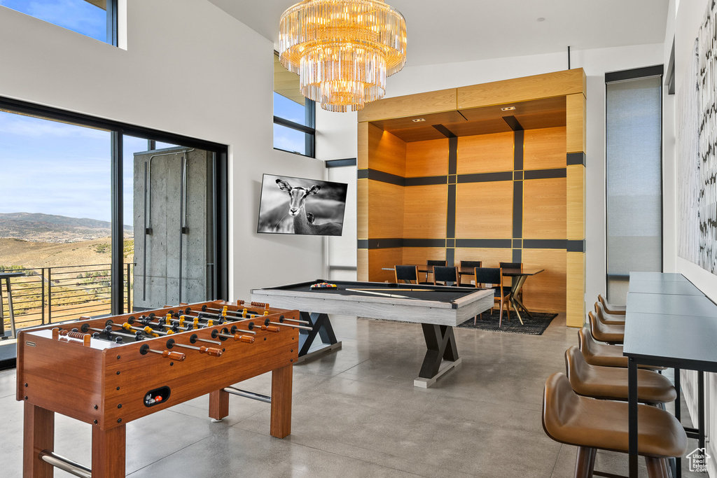 Recreation room with finished concrete flooring, a high ceiling, a chandelier, and billiards