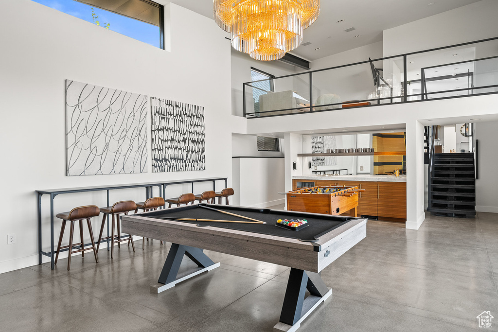 Rec room with a high ceiling, a dry bar, finished concrete flooring, a chandelier, and billiards