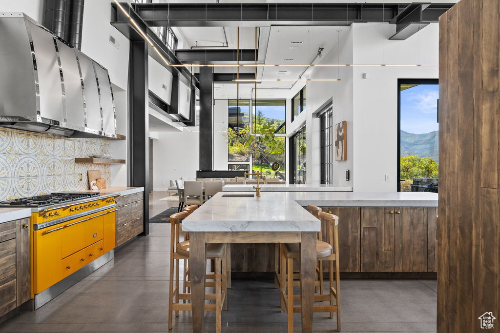 Kitchen with finished concrete flooring, gas stovetop, decorative backsplash, a high ceiling, and wall chimney range hood