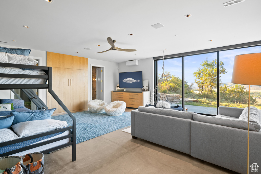 Living room featuring finished concrete flooring, a ceiling fan, a wall of windows, and a wall mounted air conditioner