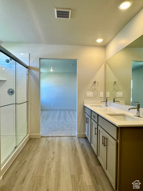 Bathroom featuring wood-type flooring, vanity, a shower with shower door, and a textured ceiling