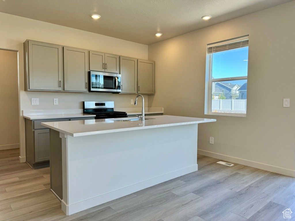 Kitchen with appliances with stainless steel finishes, a center island with sink, sink, and light hardwood / wood-style flooring