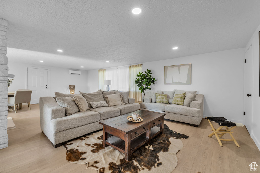 Living room with an AC wall unit, light wood-type flooring, and a textured ceiling