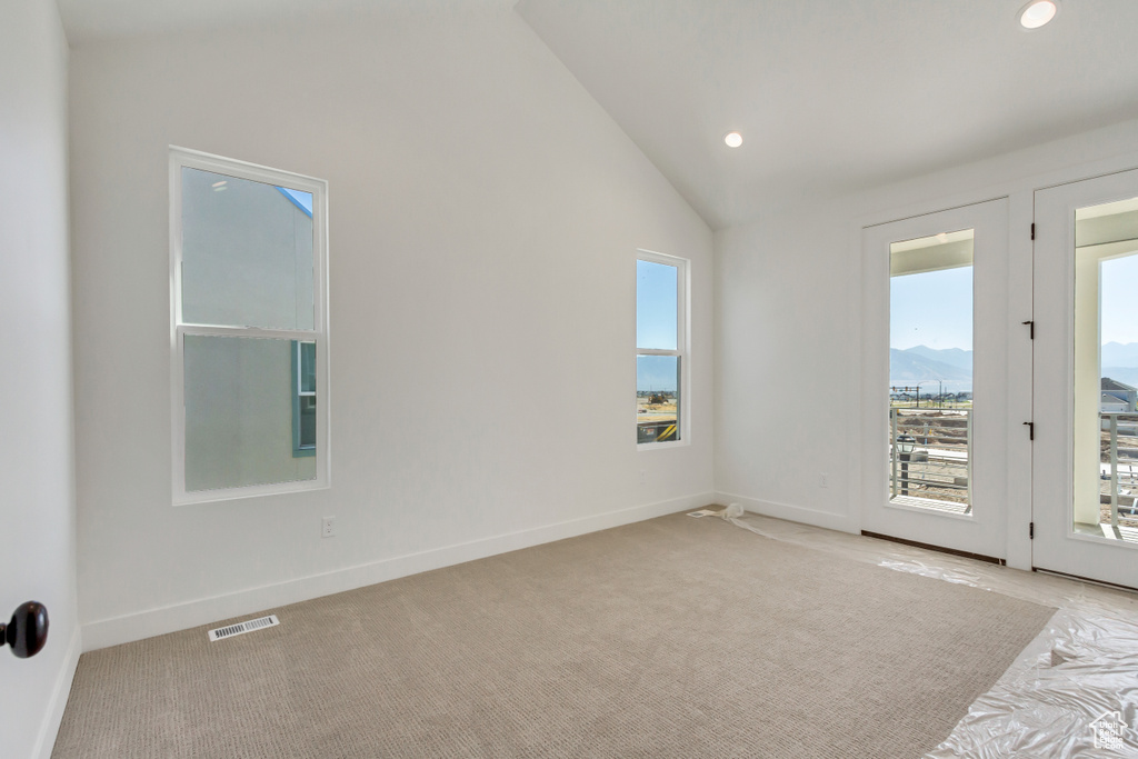 Carpeted empty room featuring a mountain view, lofted ceiling, and a healthy amount of sunlight