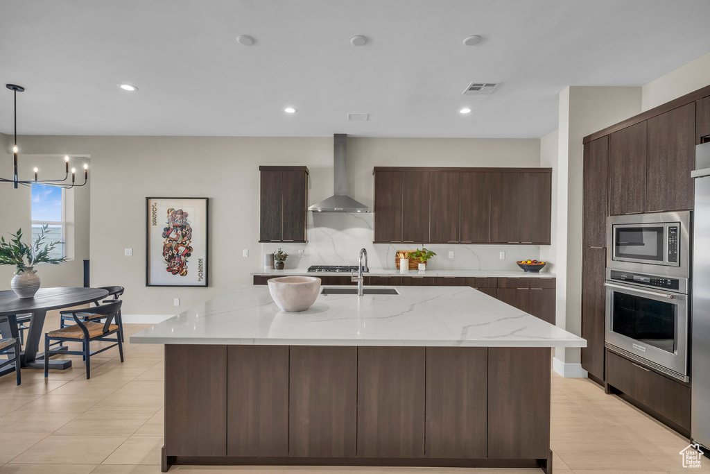 Kitchen with wall chimney exhaust hood, stainless steel appliances, hanging light fixtures, and a kitchen island with sink