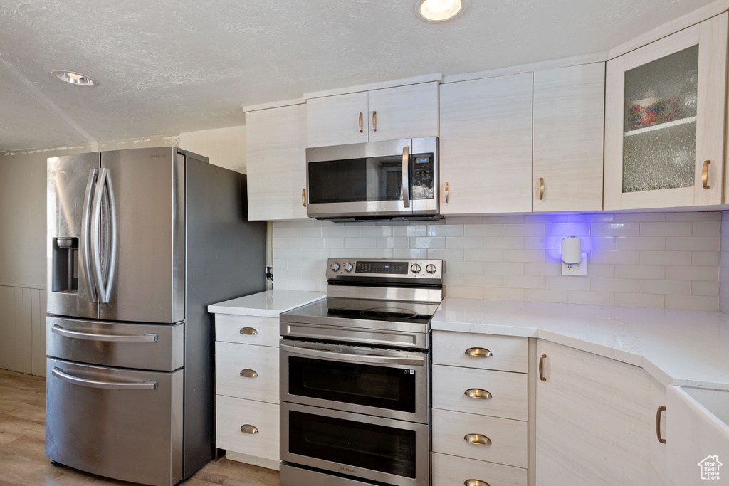 Kitchen with a textured ceiling, light wood-type flooring, appliances with stainless steel finishes, and decorative backsplash