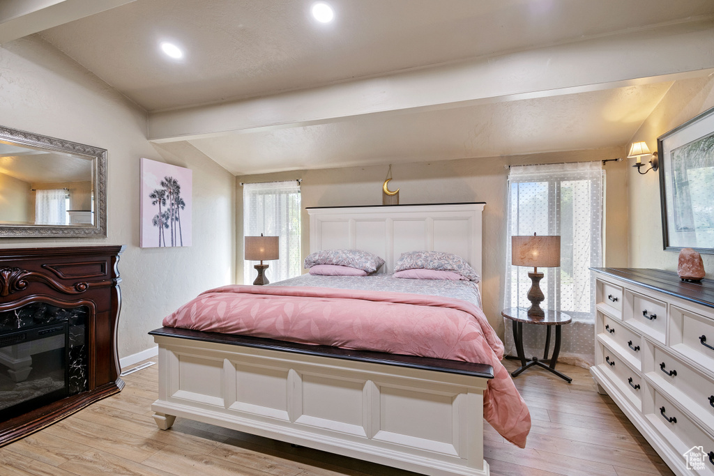 Bedroom with light wood-type flooring, multiple windows, a fireplace, and vaulted ceiling with beams