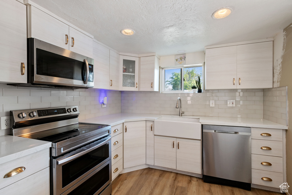 Kitchen with appliances with stainless steel finishes, decorative backsplash, light hardwood / wood-style floors, and sink