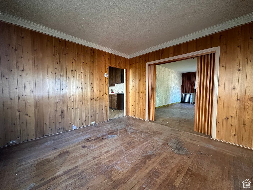 Empty room featuring radiator, hardwood / wood-style flooring, wooden walls, and crown molding