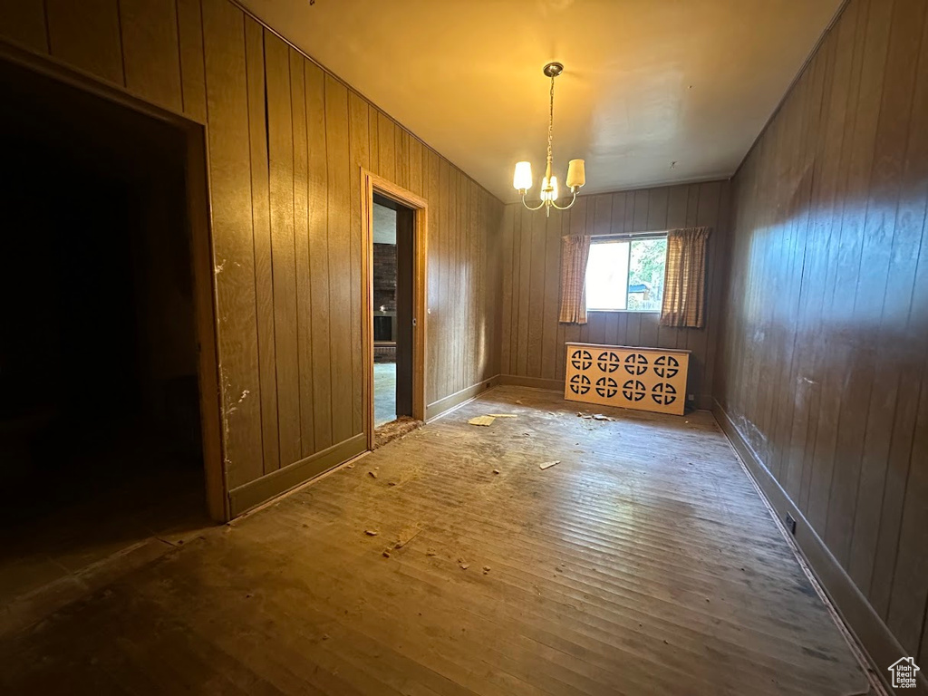 Spare room featuring an inviting chandelier, wooden walls, and hardwood / wood-style floors