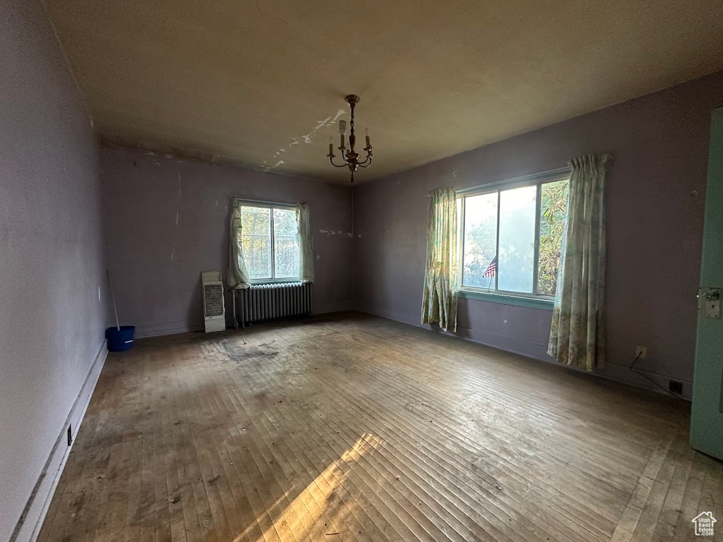 Unfurnished room with radiator, hardwood / wood-style flooring, a notable chandelier, and a healthy amount of sunlight