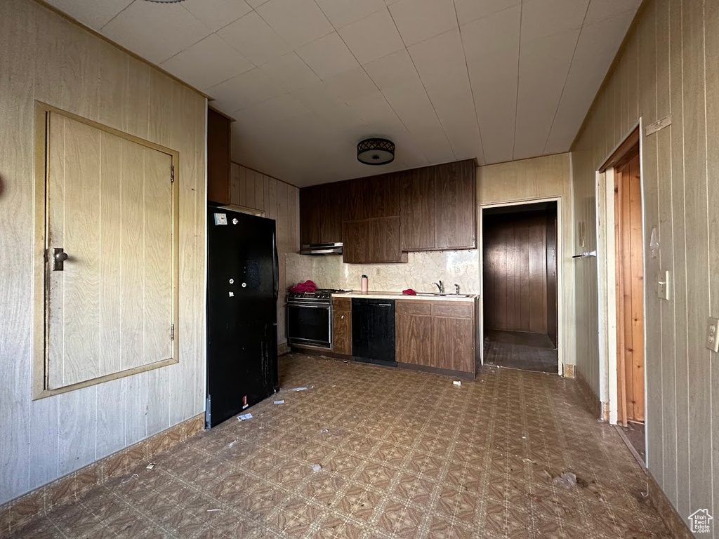 Kitchen featuring wood walls, black appliances, dark brown cabinets, sink, and extractor fan