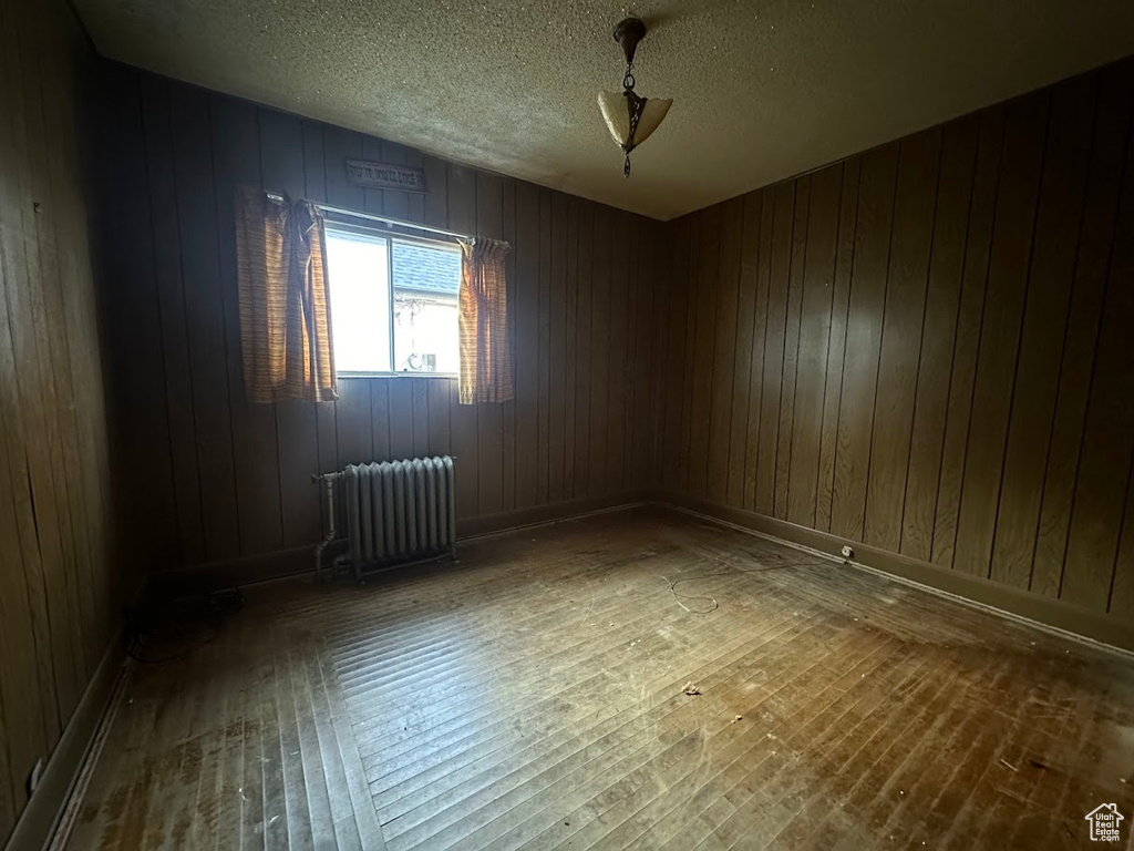 Unfurnished room with wood-type flooring, a textured ceiling, wooden walls, and radiator heating unit