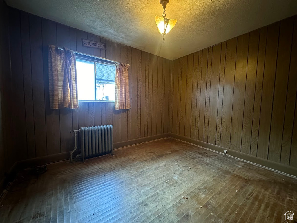 Unfurnished room featuring radiator, wood walls, a textured ceiling, and hardwood / wood-style floors