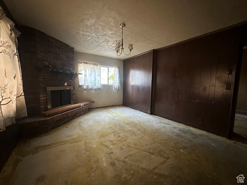 Unfurnished living room with a textured ceiling, a fireplace, wood walls, and an inviting chandelier