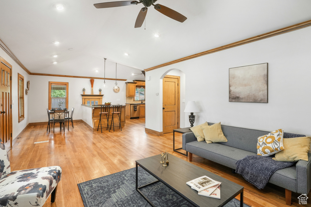 Living room featuring light wood-type flooring, crown molding, vaulted ceiling, and ceiling fan