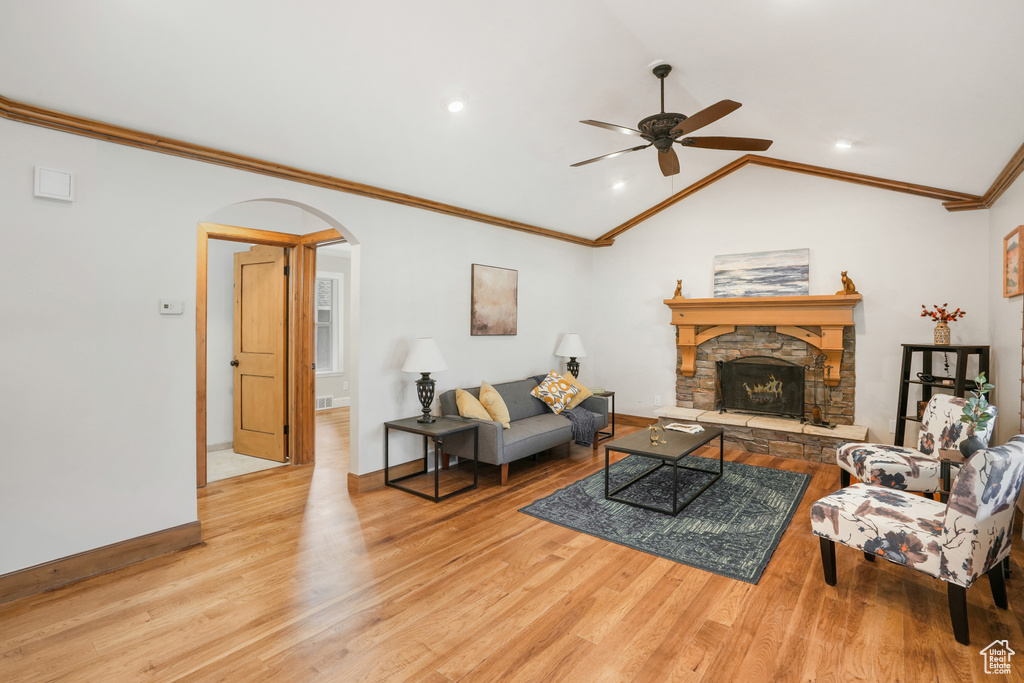 Living room with light hardwood / wood-style floors, a stone fireplace, crown molding, lofted ceiling, and ceiling fan